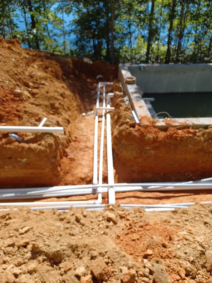 White plumbing lines laid in an open trench of red clay on a new-construction job site